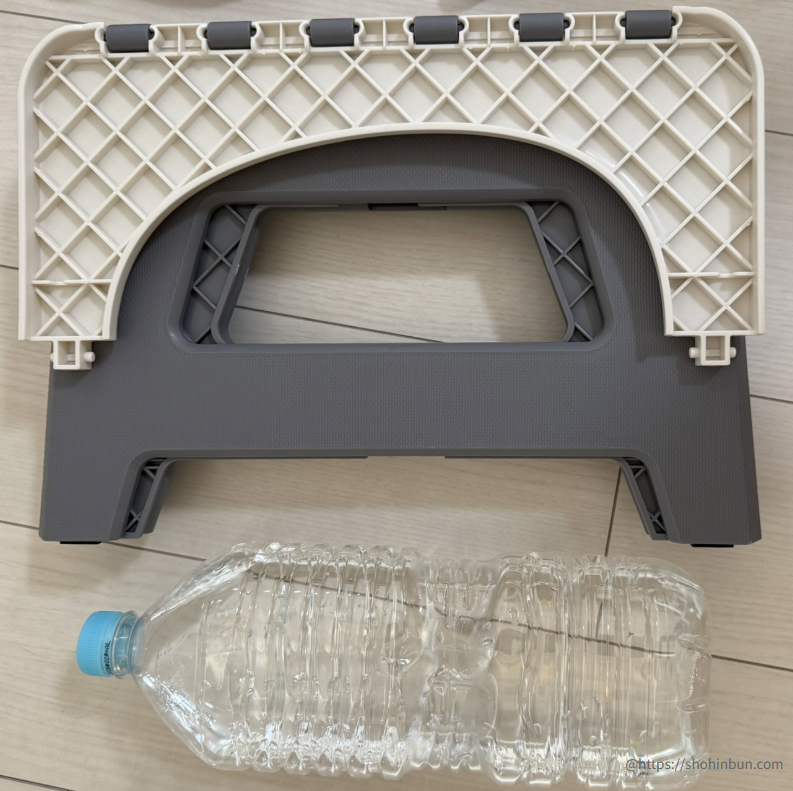 折りたたみトイレ「スツーレ（Stoole）」を畳んだ状態と、2Lペットボトルを並べたサイズ比較。厚みと横幅がペットボトルとほぼ同等で、非常にコンパクトに収納できることがわかります。